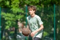 Teenager playing basketball smiling, cheerful. Fit boy with basketball ball outdoors. Kid dribbling the ball at the court Royalty Free Stock Photo