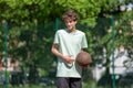 Teenager playing basketball smiling, cheerful. Fit boy with basketball ball outdoors. Kid dribbling the ball at the court Royalty Free Stock Photo