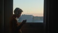 Teenager playing phone at sunrise