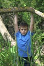 A teenager poses for a photographer while walking in the park. Hanging, clutching the tree like a crossbar.