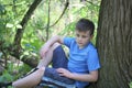 A teenager poses for a photographer while walking in the park. Sits, leaning on a tree.