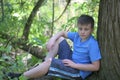 A teenager poses for a photographer while walking in the park. Sits, leaning on a tree.