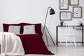 Teenager`s artistic bedroom interior with framed drawings above a make-up table and a comfortable bed dressed in burgundy linen a