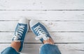 Teenager`s feet in blue color casual new sneakers with white shoelaces on the white wooden floor close up image. Vintage style in Royalty Free Stock Photo