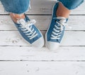 Teenager`s feet in blue color casual new sneakers with white shoelaces on the white wooden floor close up image. Vintage style in