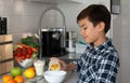 A teenager schoolboy prepares breakfast for himself pours cereal into a bowl alone in the kitchen Royalty Free Stock Photo