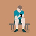 A teenager in shorts and a blue shirt sits and bent over a gadget and holds a smartphone in his hands.