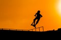 Teenager silhouette showing high jump tricks on scooter against orange sky Royalty Free Stock Photo