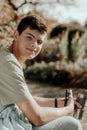 A Teenager Sits On A Bench In The Autumn Park Drinks Coffee From A Thermo Mug And Looks Into A Phone. Portrait Of