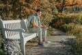 A Teenager Sits On A Bench In The Autumn Park Drinks Coffee From A Thermo Mug And Looks Into A Phone. Portrait Of