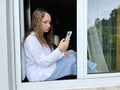 A Girl In A White Shirt A Teenager Sits On A White Windowsill The View From The Street She Can Be Seen In The Window In