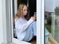 a girl in a white shirt a teenager sits on a white windowsill the view from the street she can be seen in the window in