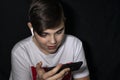 a teenager sits in the dark with a smartphone and headphones and looks enthusiastically at the phone. the problem of children`s e