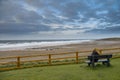 Teenager sitting on a bench looking at beautiful Fanore beach. Ireland. Blue cloudy sky and Atlantic ocean. Travel and tourism