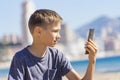 Teenager sitting at city beach using his phone. Boy looking to cell phone screen, reading, playing games, chat, watching Royalty Free Stock Photo