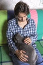 A teenager is sitting on the couch and stroking a Scottish cat sleeping on his lap Royalty Free Stock Photo