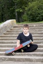 A teenager with a skateboard. Sits with a skateboard against the backdrop of a stone staircase.