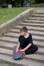 A teenager with a skateboard. Sits with a skateboard against the backdrop of a stone staircase.