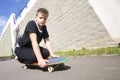 A teenager with a skateboard. Sits on a skateboard.