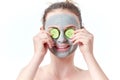 Teenager skincare concept. Young teen girl with dry clay facial mask covering her eyes with two slices of cucumber smiling Royalty Free Stock Photo