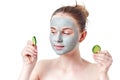 Teenager skincare concept. Young teen girl with dry clay facial mask holding two slices of cucumber