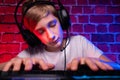 A teenager sleeps at the keyboard. A gamer boy plays computer games against a neon lit brick wall