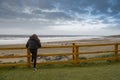 Teenager standing by wooden barrier and looking at beautiful Fanore beach. Ireland. Blue cloudy sky and Atlantic ocean. Travel and