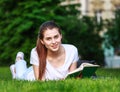 Teenager student girl lying on grass in park near university reading book outdoors Royalty Free Stock Photo