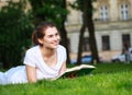 Teenager student girl lying on grass in park near university reading book outdoors Royalty Free Stock Photo