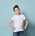 Teenager with stylish haircut, dressed in white t-shirt. Smiling, folded his hands and looking up, posing against blue background