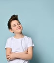 Teenager with stylish haircut, dressed in white t-shirt. Smiling, folded his hands and looking up, posing against blue background