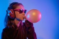 Teenager in sunglasses listening music with headphones in trendy neon light. Emotional portrait millennial pretty girl