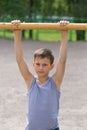 A teenager in a T-shirt is engaged in gymnastics on a horizontal bar