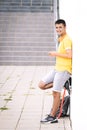 Teenager waiting leaning on the wall in a yellow shirt, with a skateboard and backpack