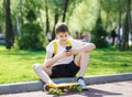 Teenager in white t shirt spends free time training skating in the city park. Boy looking on mobile phone. Royalty Free Stock Photo