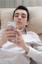 Teenager young man lying on sofa at home, holding and using smart phone Royalty Free Stock Photo