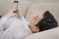 Teenager young man lying on sofa at home, holding and using smart phone Royalty Free Stock Photo