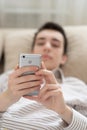 Teenager young man lying on sofa at home, holding and using smart phone Royalty Free Stock Photo