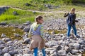 Teenagers with backpacks cautiously cross the creek along the rocks, hiking into the forest. Summer vacation. Royalty Free Stock Photo