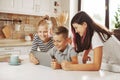 Teenagers, girls and boys, are sitting with a tablet at the table in the home kitchen, chatting on video with friends on