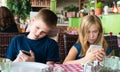 Teenagers having fun with mobile phones in cafe. Modern lifestyle and technology concept. Children sitting in restaurant and Royalty Free Stock Photo
