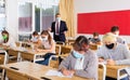 Teenagers in protective masks studying in classroom with teacher