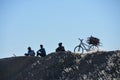 3 teenagers resting on a hill in a rural area with a bike loaded with fire wood