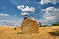 Teenagers in shorts and T-shirts jump on haystacks. Wheat hay on an agricultural field. Royalty Free Stock Photo