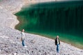 Teenagers stand on stones on the bank of the lake, which reflects the forest, hiking in the forest. Summer vacation. Royalty Free Stock Photo