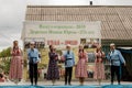 Teenagers in traditional Tatar clothes sing on stage against the backdrop of a stand with historical photographs. Holiday village