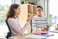 Teens latin girl and Asian guy talking using smartphones together in classroom. Royalty Free Stock Photo