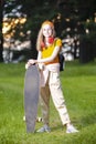 Teens Lifestyle. Relaxing Caucasian Teenager In Red Wireless Headphones and Longboard Posing in Casual Outfit On Slope in Green