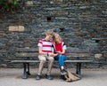 Teens sitting on the old bench against stone wall outdoors and using sharing smart phone watching video or social nets Royalty Free Stock Photo