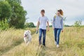 Teens walking with white dog in meadow on sunny day Royalty Free Stock Photo